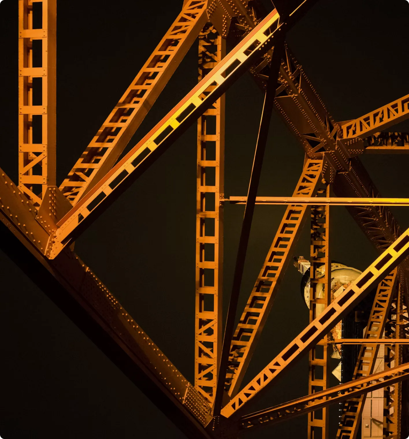Close-up of illuminated orange steel girders and beams forming a bridge structure at night.