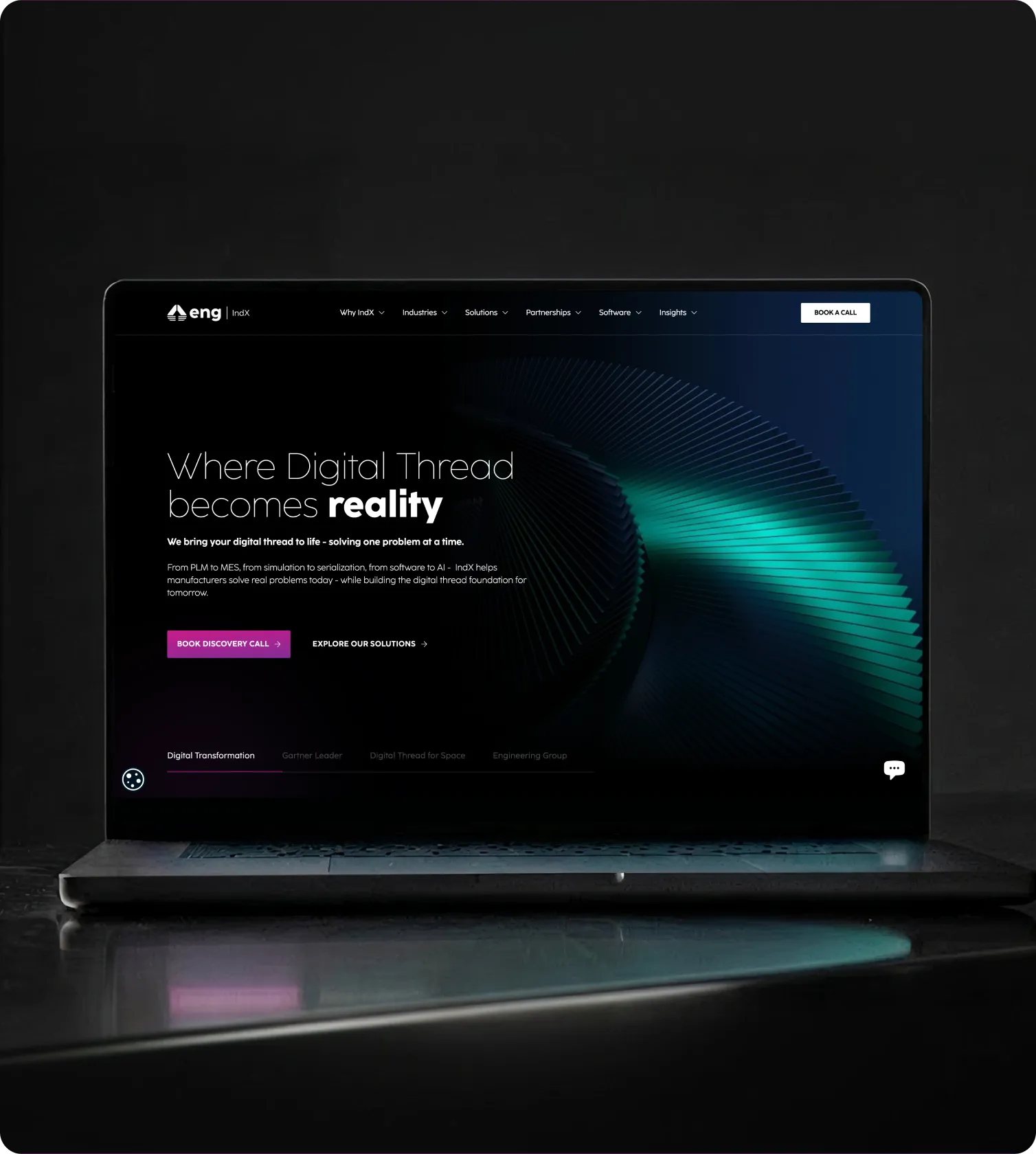Laptop on a dark surface displaying the IndX website homepage with text about bringing digital thread to reality and call-to-action buttons.