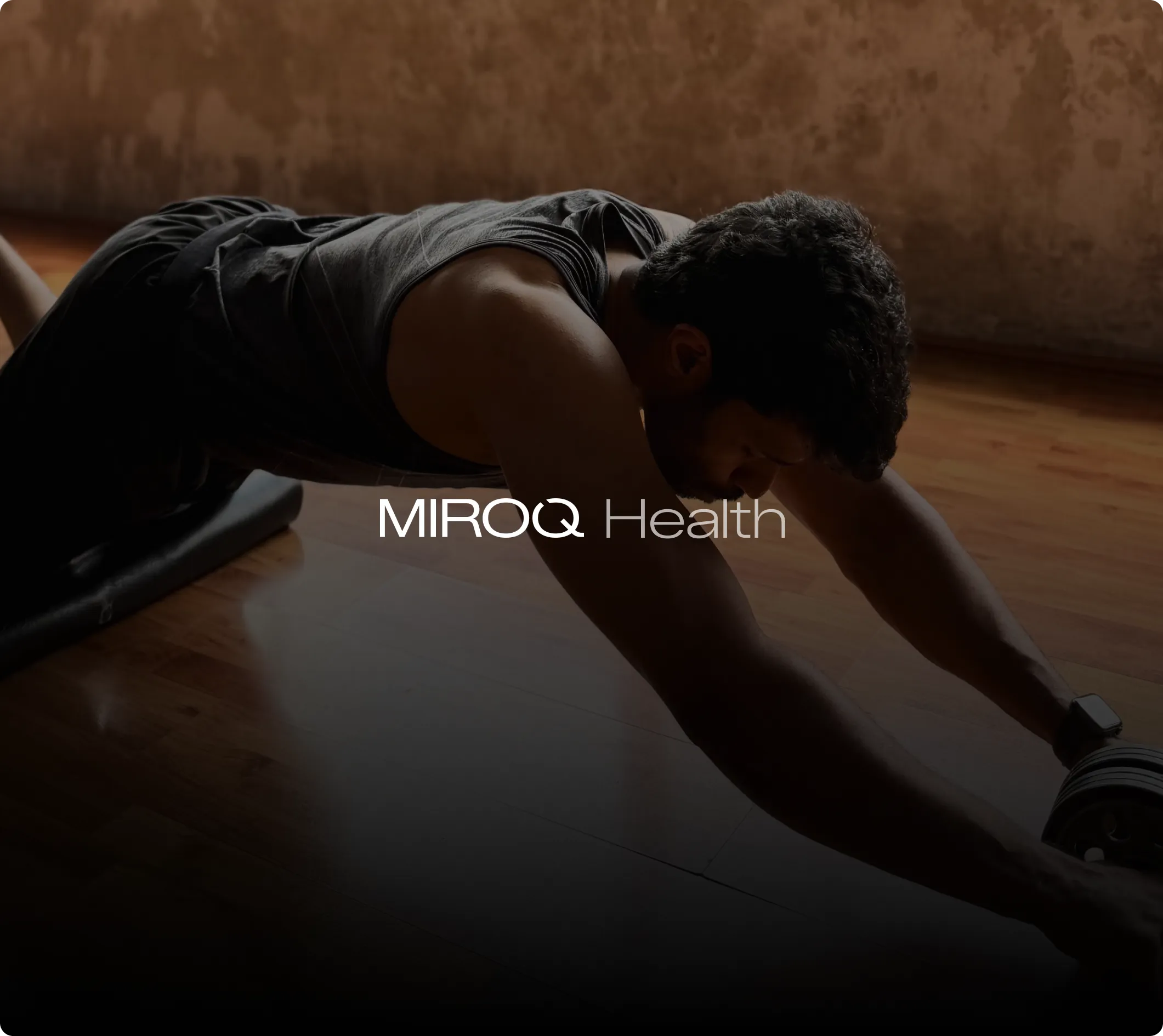 Man in a black tank top performing an ab wheel rollout exercise on a wooden floor.
