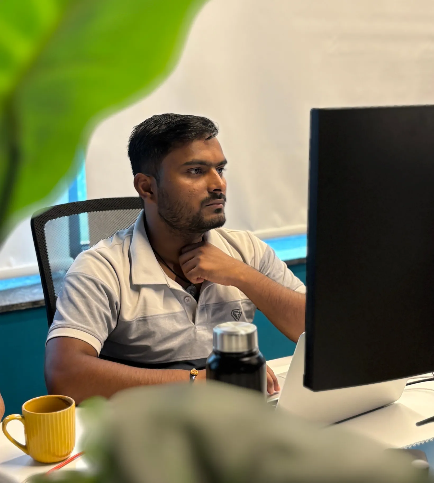 Man in white shirt working at a desk with a computer monitor, water bottle, and yellow mug nearby.