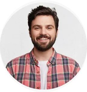 Smiling bearded man wearing a red plaid shirt over a white tee with a gray background.