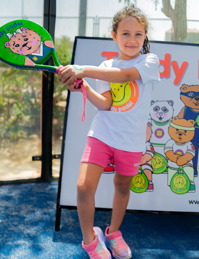 Young girl in sportswear holding a colorful paddle in a paddel court with cartoon animal backdrop.