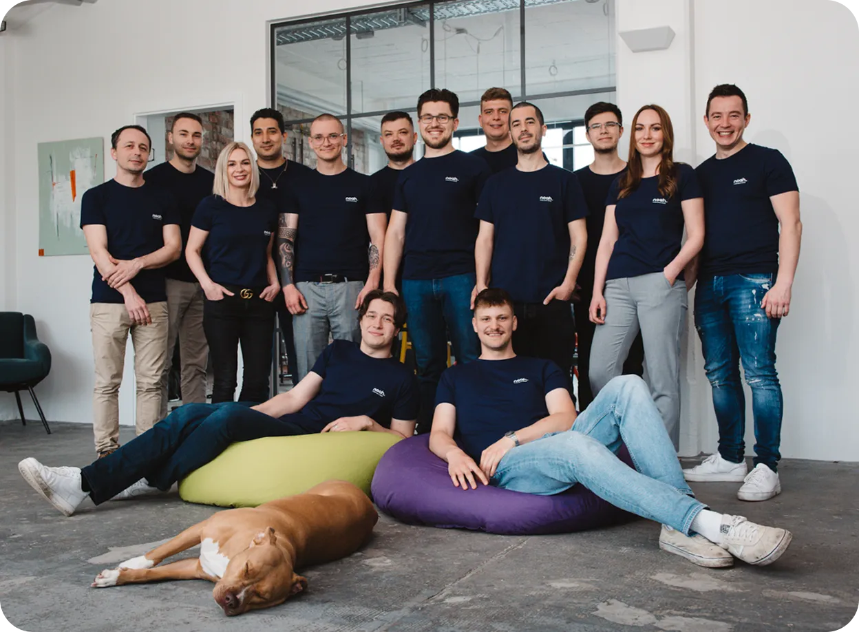 Gruppenfoto von zwölf Personen in dunkelblauen T-Shirts, zwei sitzen auf bunten Sitzsäcken, und ein Hund liegt schlafend auf dem Boden.