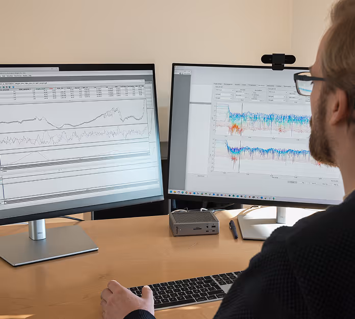 Person wearing glasses working at a desk with two monitors displaying data graphs and charts.