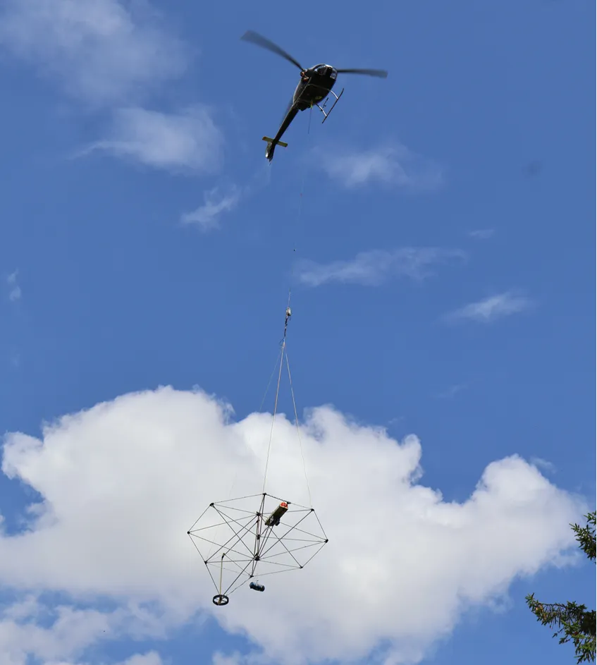 Helicopter flying in blue sky carrying a large metal structure suspended by cables.