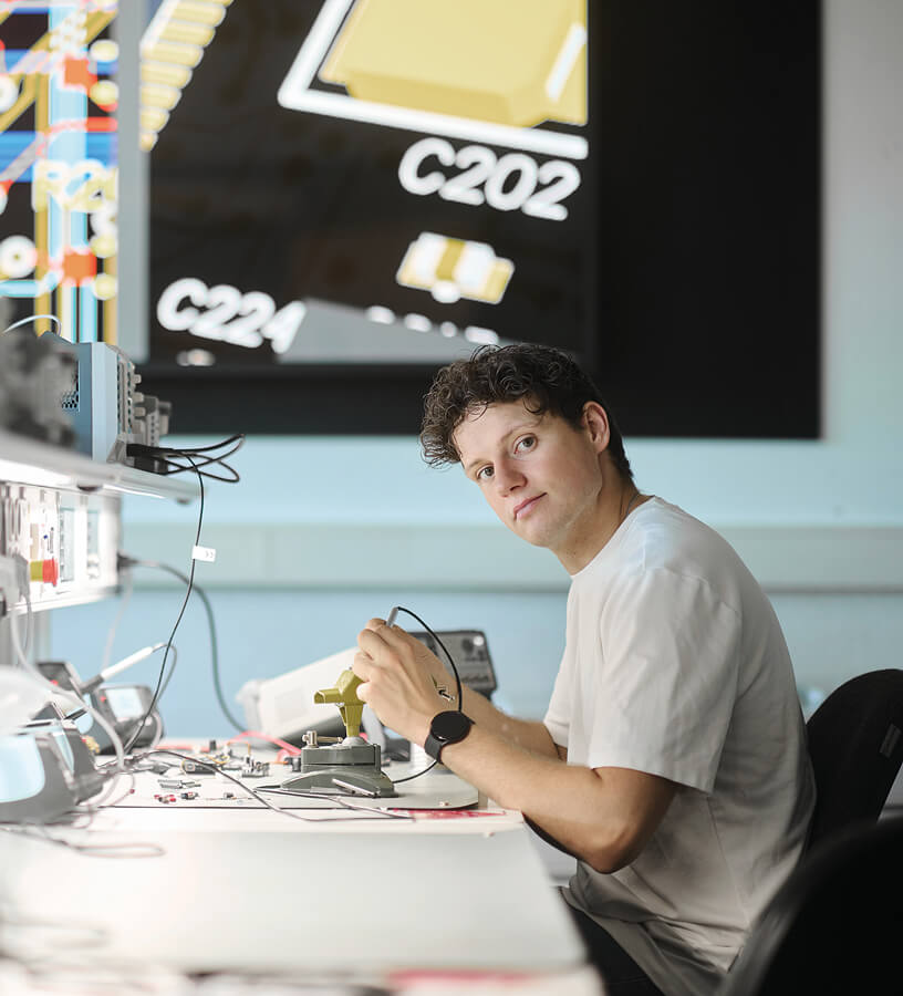 student, aged 18-20,  workstation, soldering iron in his hand.  
