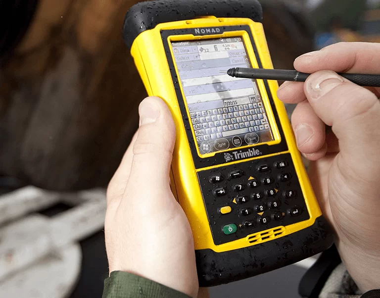 Ръка с писалка работи с жълт GPS приемник Trimble модел Nomad под дъжд.
