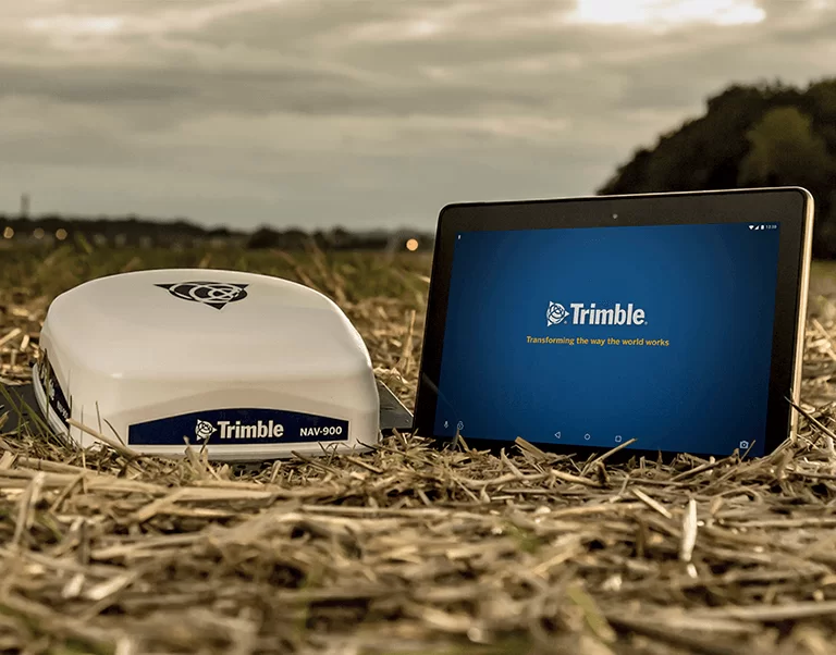 Навигационно устройство Trimble NAV-900 и таблет с екрана на Trimble, поставени в поле със слама при залез.