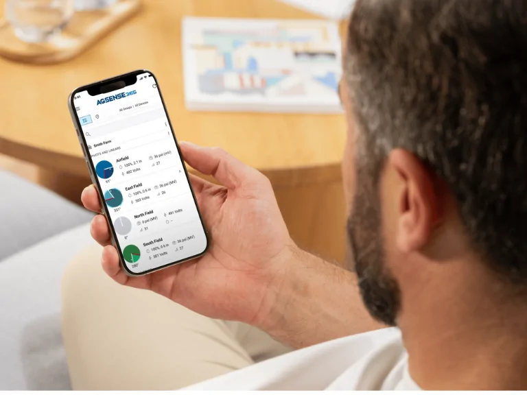 Мъж гледа приложение AGSENSE 365 на смартфон с диаграми и данни за нивата на различни полета.