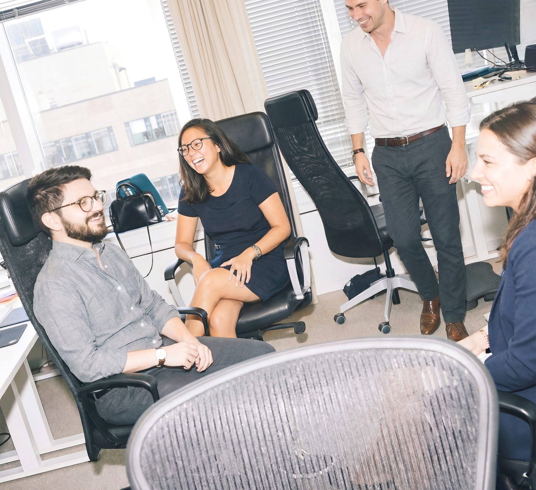 Group of six diverse coworkers gathered around a table with laptops and papers, smiling and engaged in a meeting.