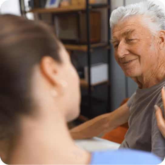 Un homme âgé souriant échange un regard avec une femme plus jeune à ses côtés dans une pièce intérieure.