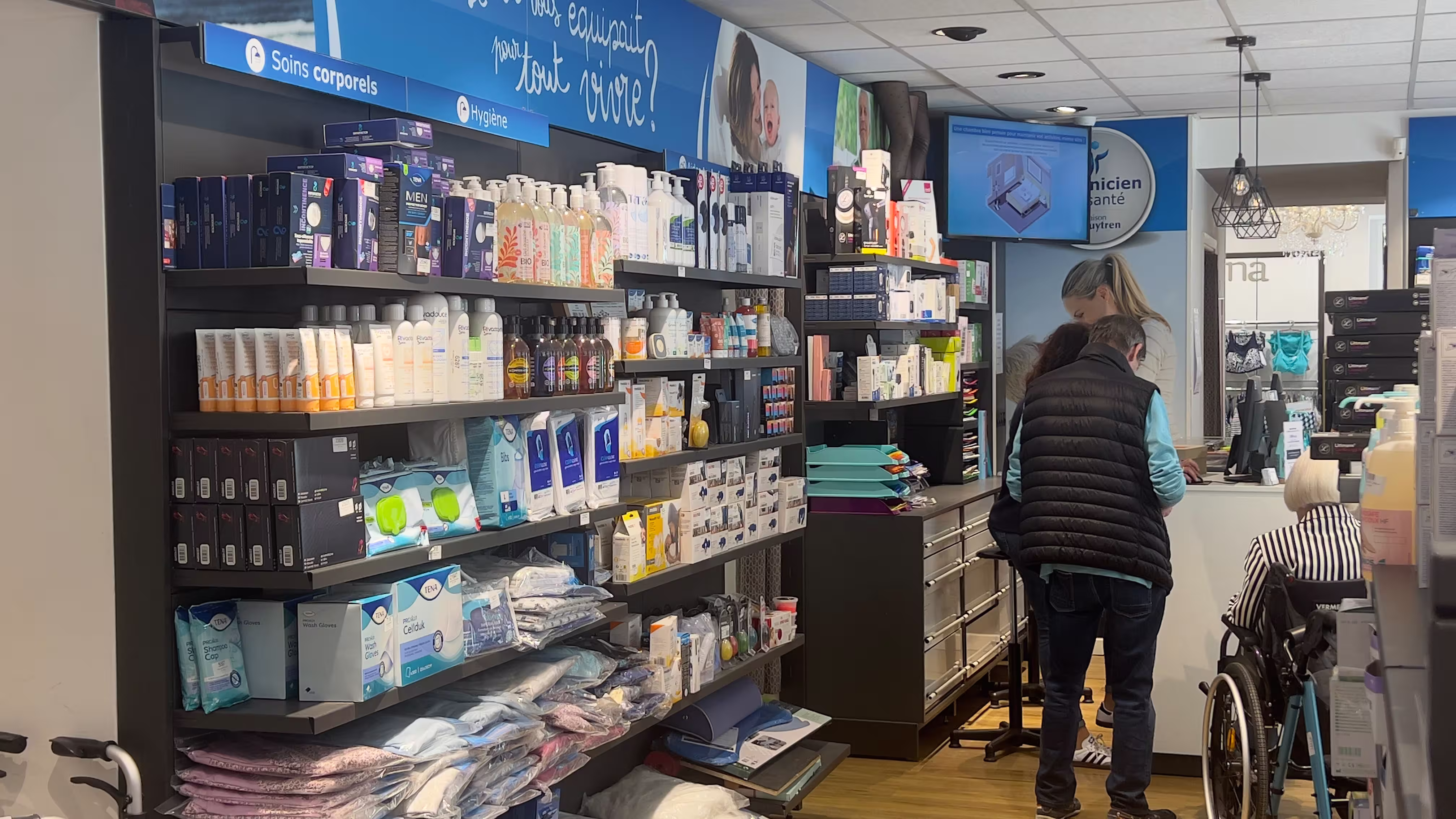 Magasin de soins corporels et hygiène avec plusieurs étagères bien remplies et des clients au comptoir, dont une personne en fauteuil roulant.