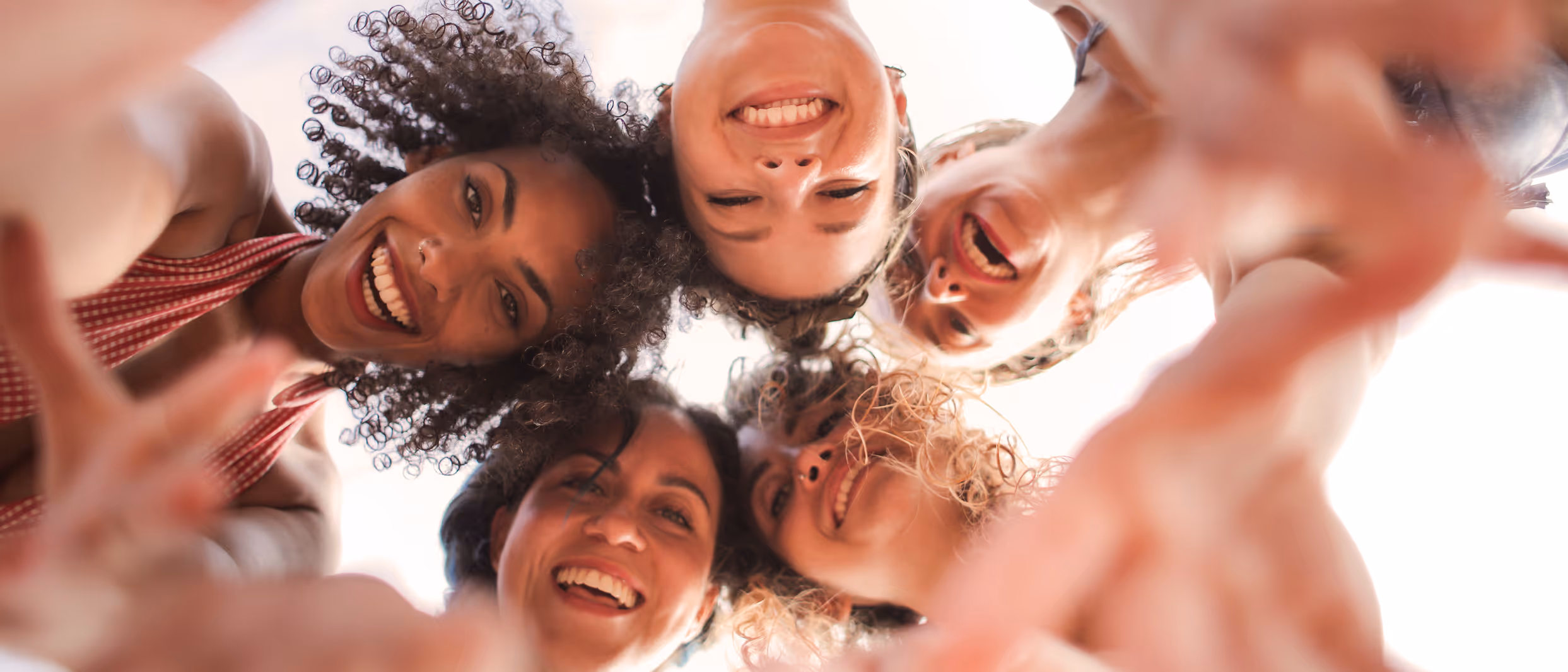 Group of five diverse women smiling and looking down at the camera in a circle.