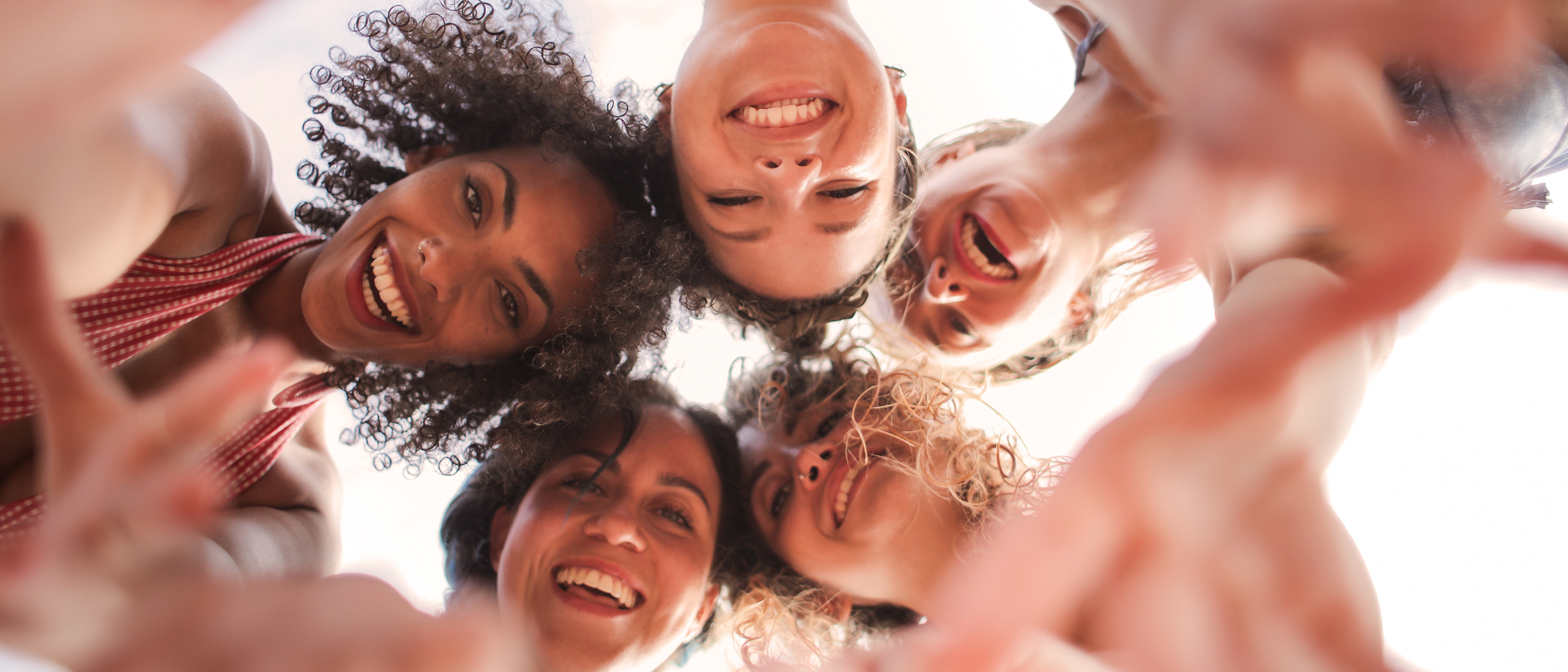 Group of five diverse women smiling and looking down at the camera in a circle.