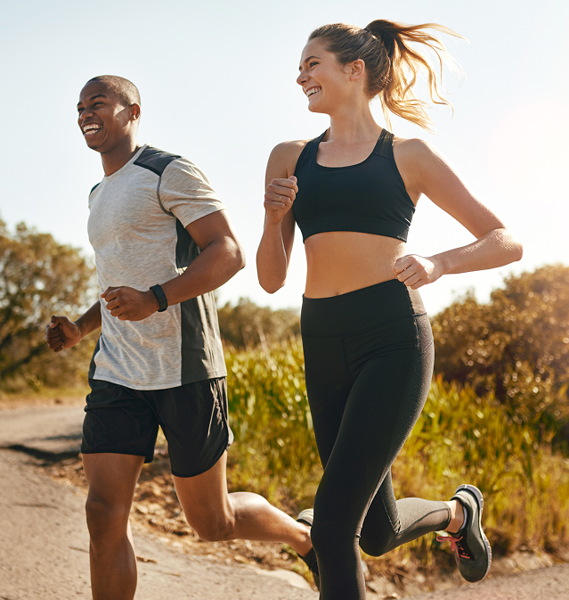 A man and a woman jogging outdoors on a sunny day, both smiling and dressed in athletic wear.
