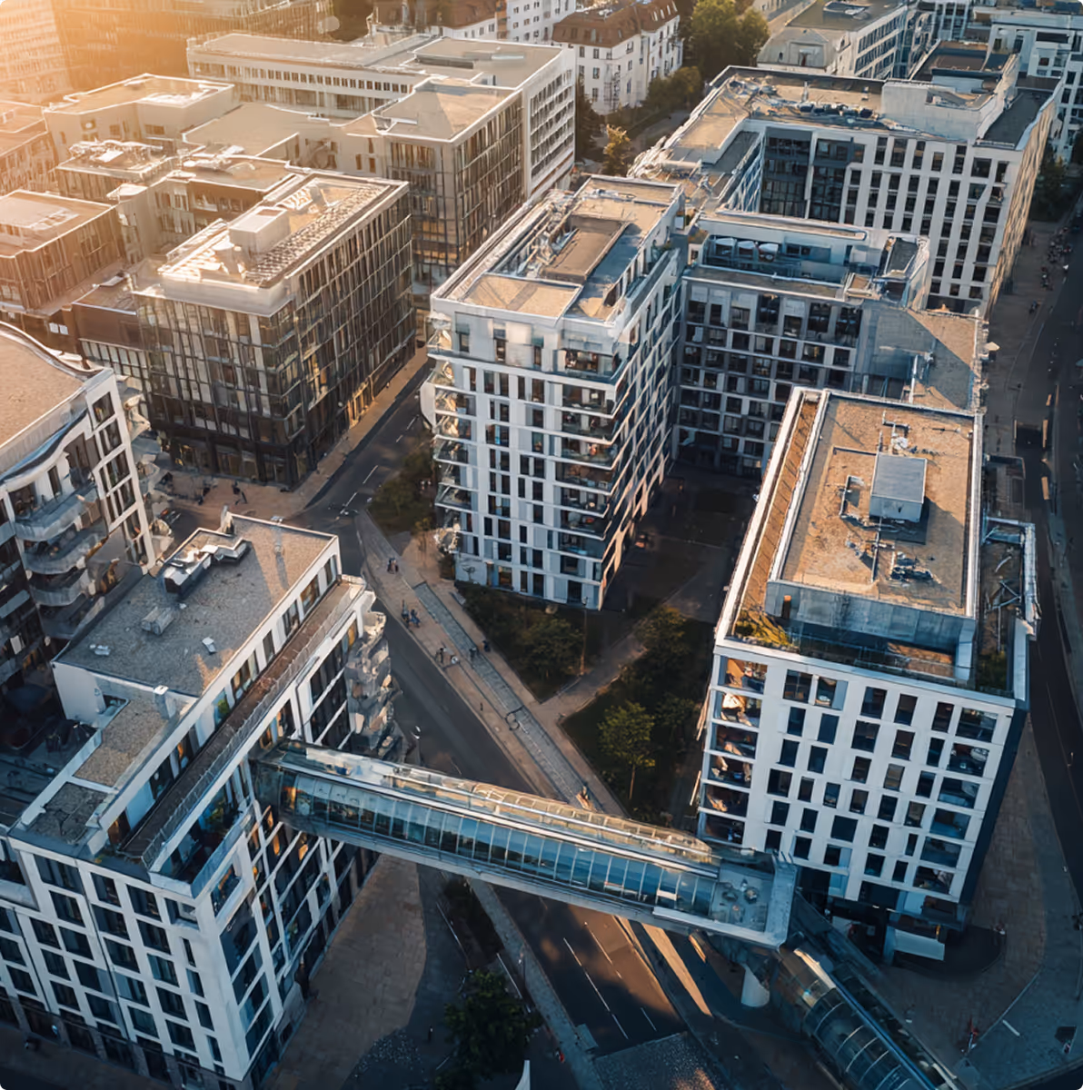Luftaufnahme moderner städtischer Gebäude, die durch eine gläserne Fußgängerbrücke verbunden sind, bei Sonnenuntergang.