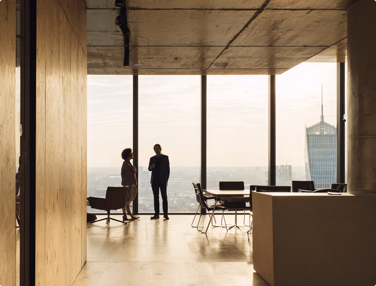 Silhouetten zweier Geschäftsleute, die sich in einem modernen Büro mit raumhohen Fenstern und Blick auf die Stadtlandschaft und Wolkenkratzer unterhalten.