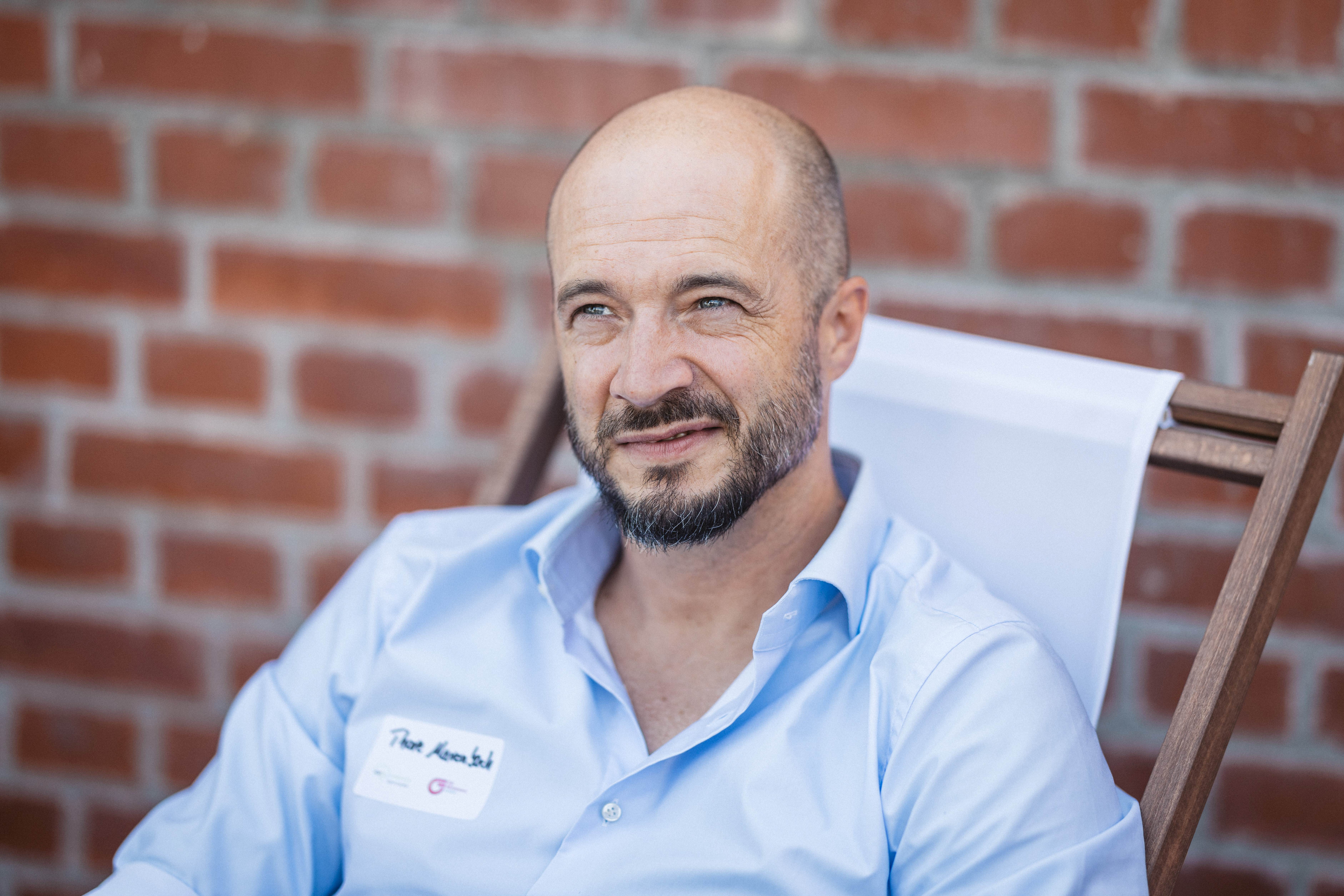 Professioneller Mann in schwarzem Anzug und Krawatte lächelt vor dunklem Hintergrund.