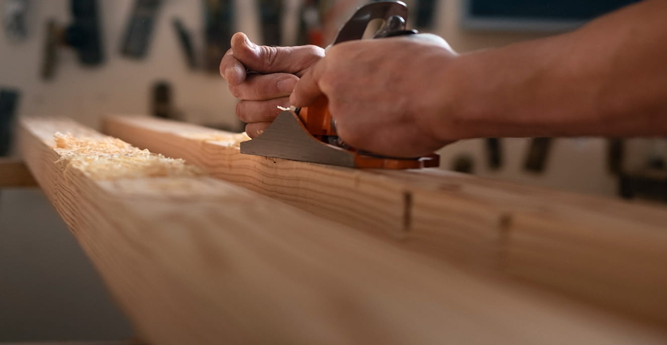 Close-up of hands planing a wooden plank with a hand plane tool.