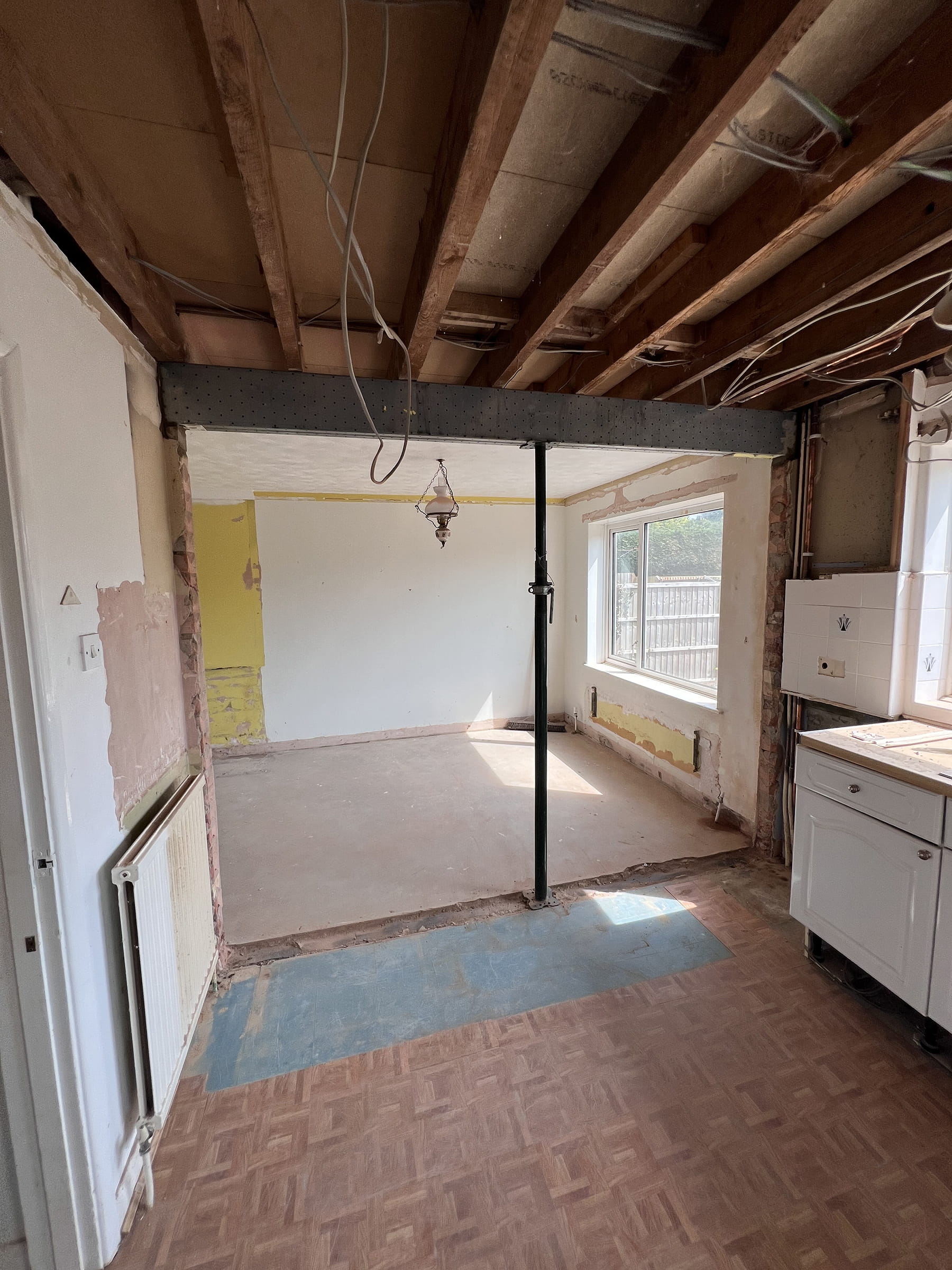 Interior room under renovation with exposed ceiling beams, a metal support beam, and unfinished walls and floor.