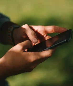 Person holding and interacting with a smartphone outdoors with blurred green background.