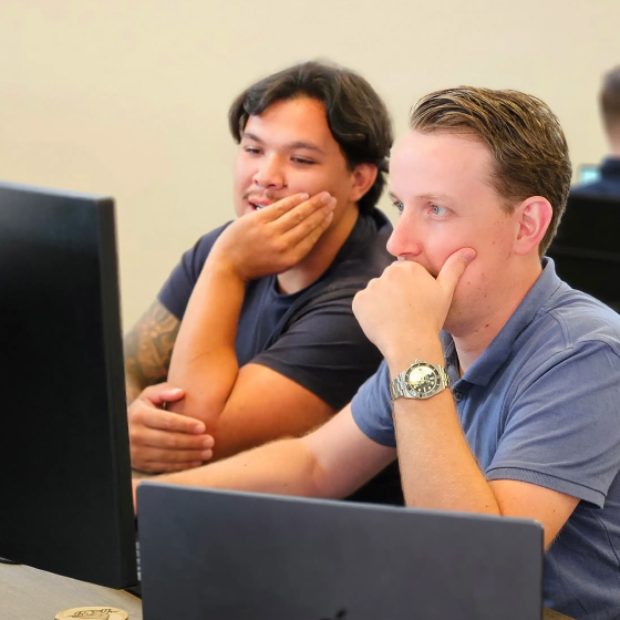 Twee mannen kijken geconcentreerd naar een computerscherm in een kantooromgeving.