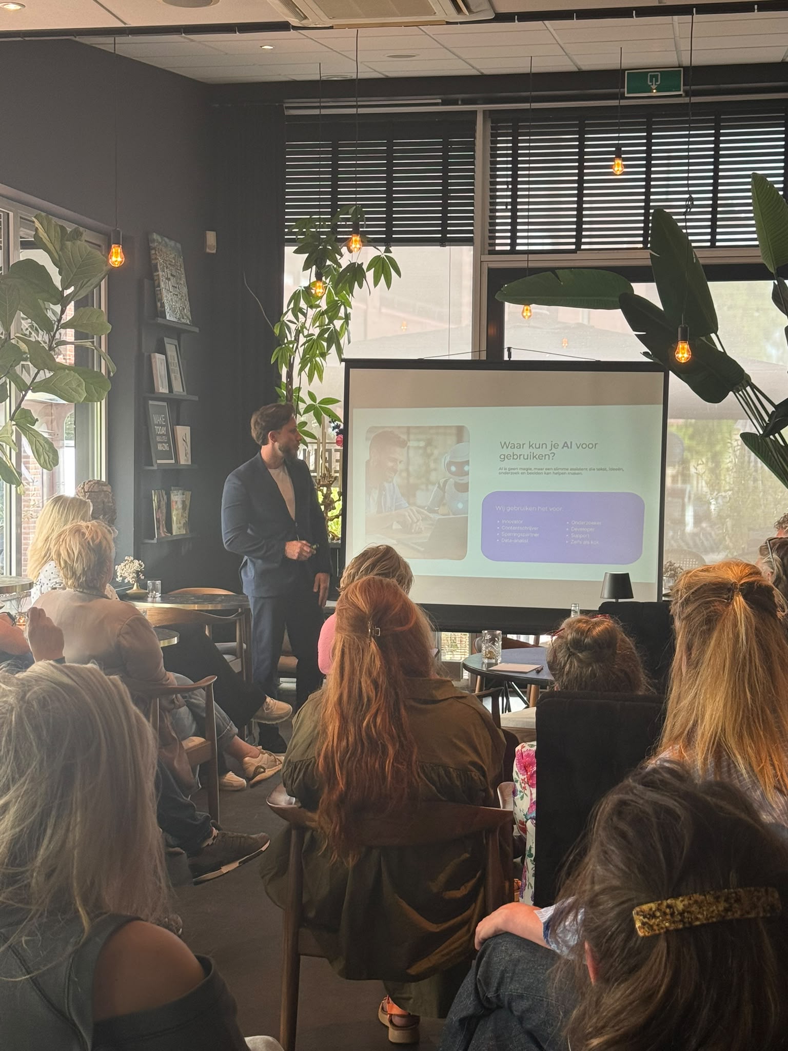 Twee mannen die lachen en praten terwijl ze aan een bureau zitten met laptops, planten ervoor en het woord 'Klikvast' op de glazen wand achter hen.