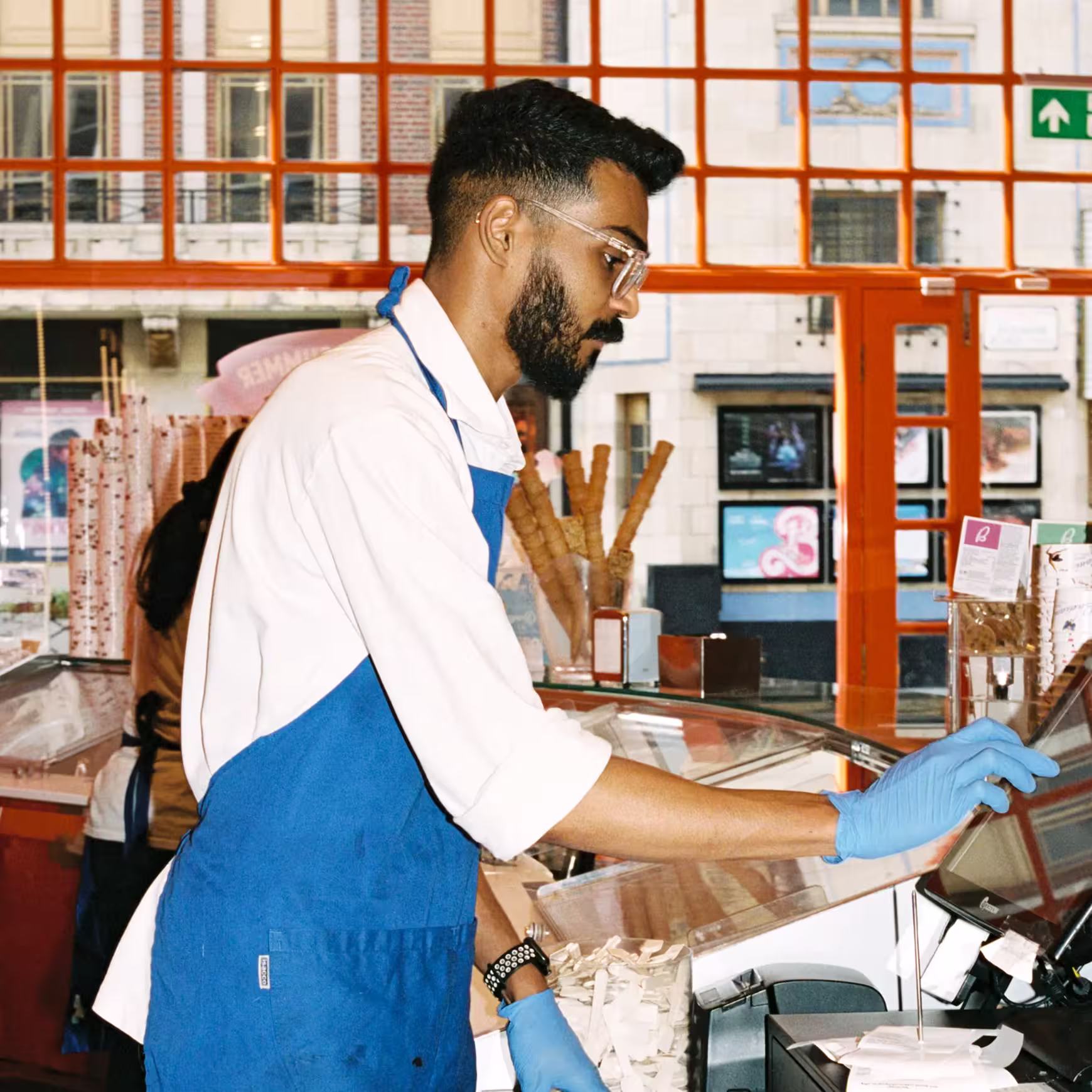 Ice cream shop team member operating a till while serving.