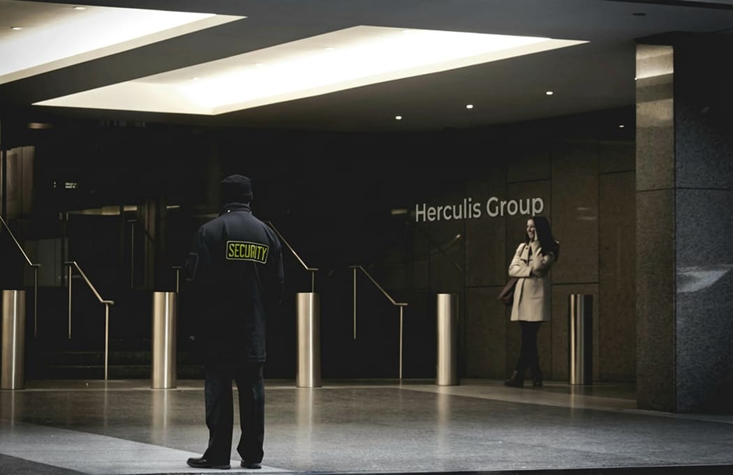 A security guard stands outside a modern office building entrance