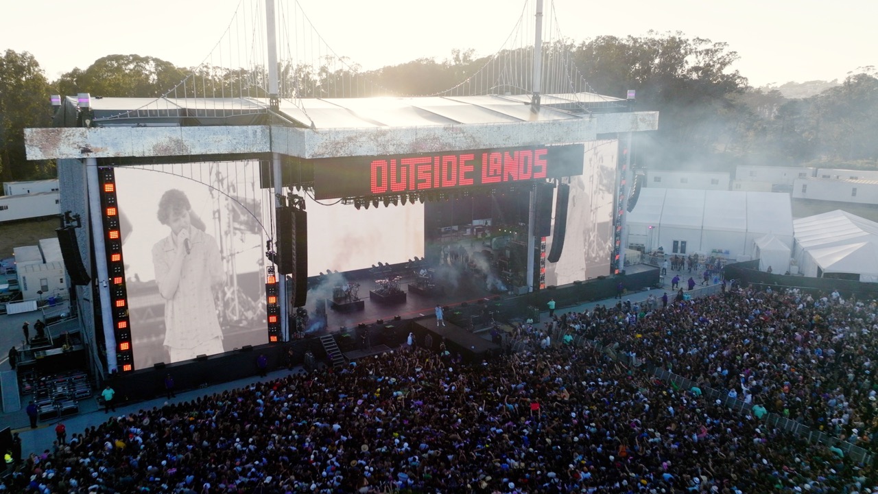 Large outdoor concert stage at Outside Lands festival with a crowd watching a performer displayed on big screens.