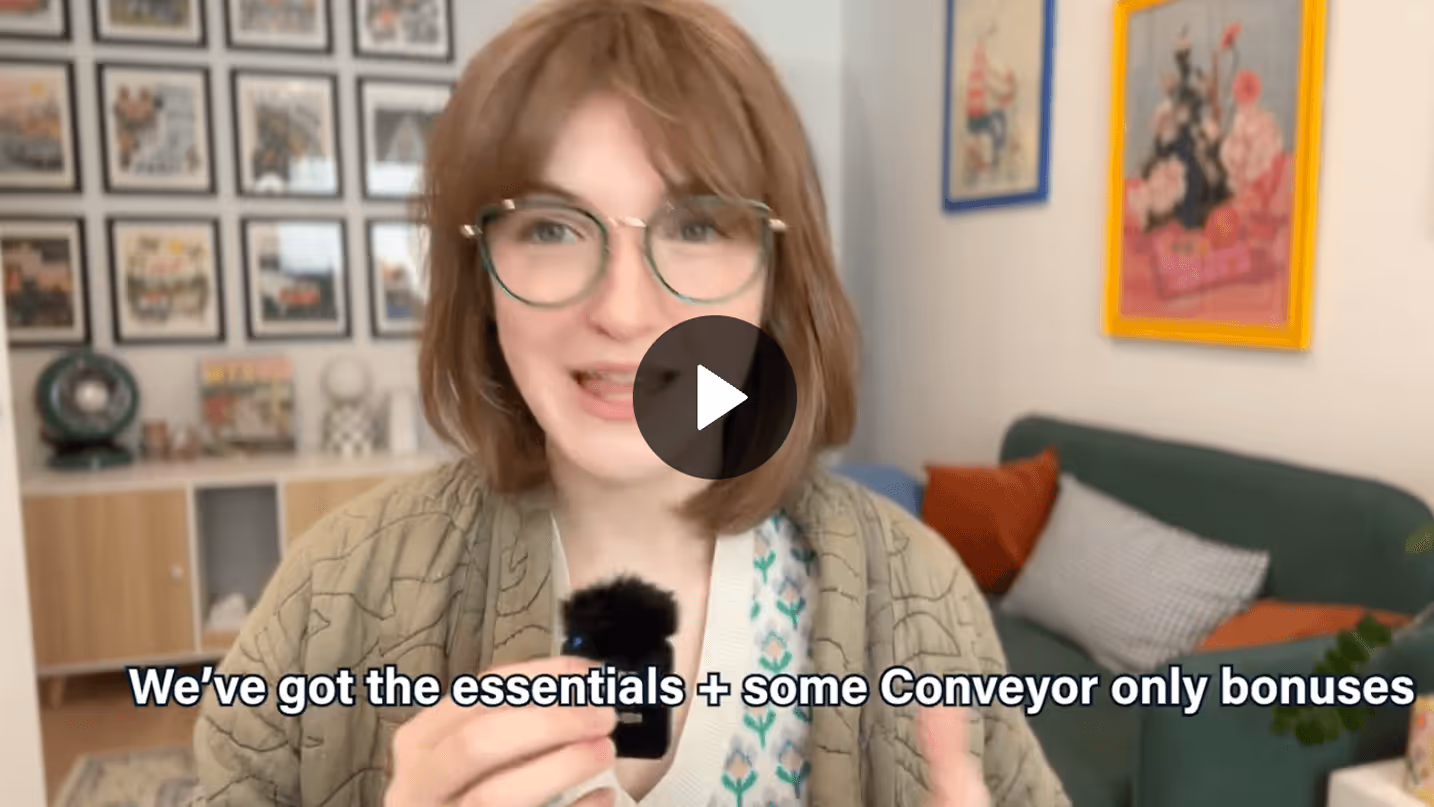 Woman with glasses speaking into a small microphone in a cozy living room with framed pictures.