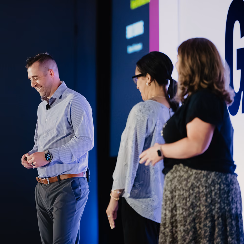 Three speakers on stage at a conference, two women and one man smiling and engaging at GiveCon