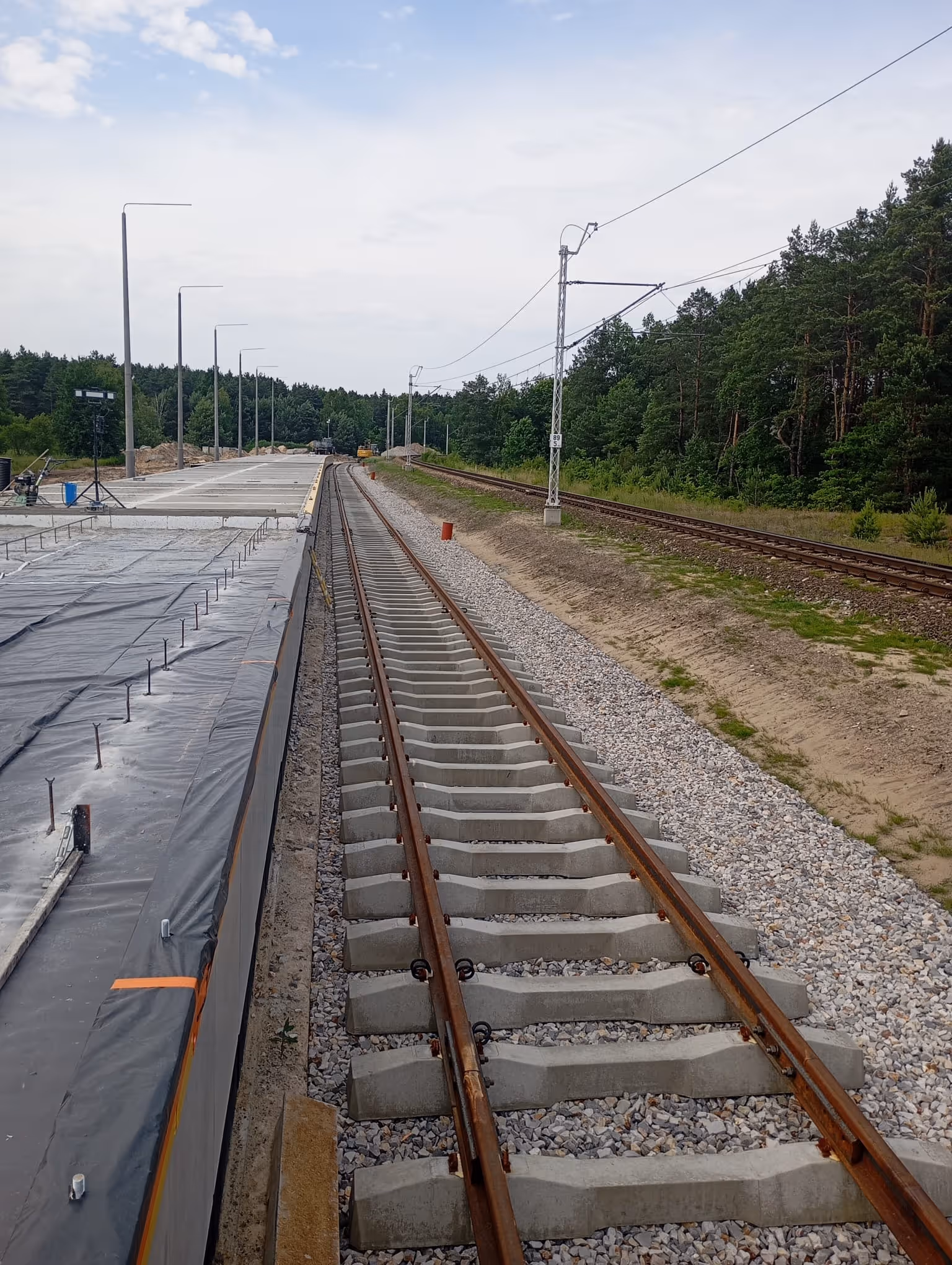 Widok na tory kolejowe i stację kolejową w lesie podczas budowy.
