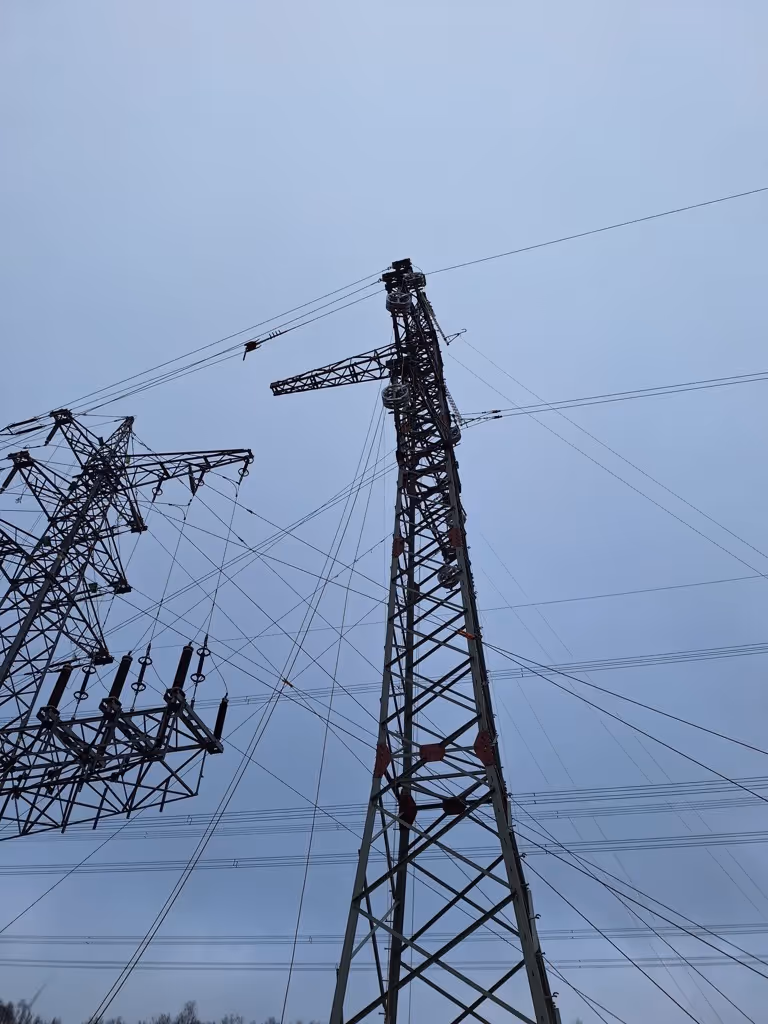 Wysokie słupy elektryczne i linie przesyłowe na tle pochmurnego nieba.