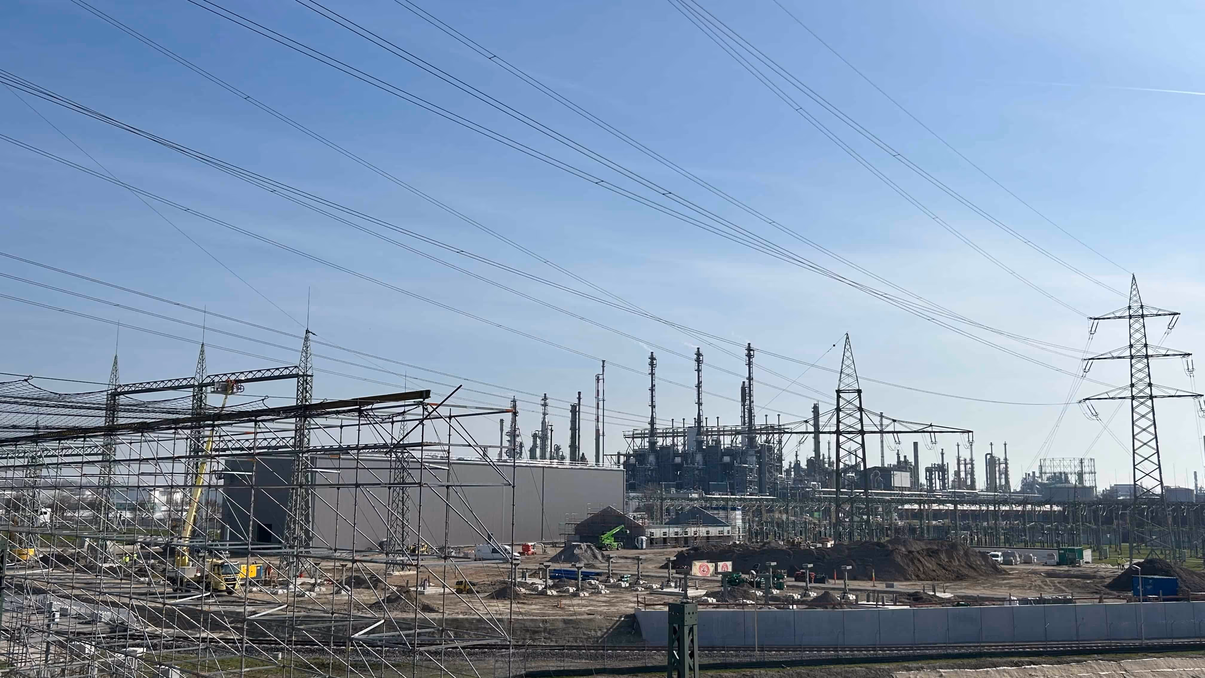 Zakład przemysłowy z licznymi rurami, kominami i konstrukcjami metalowymi pod niebieskim niebem.