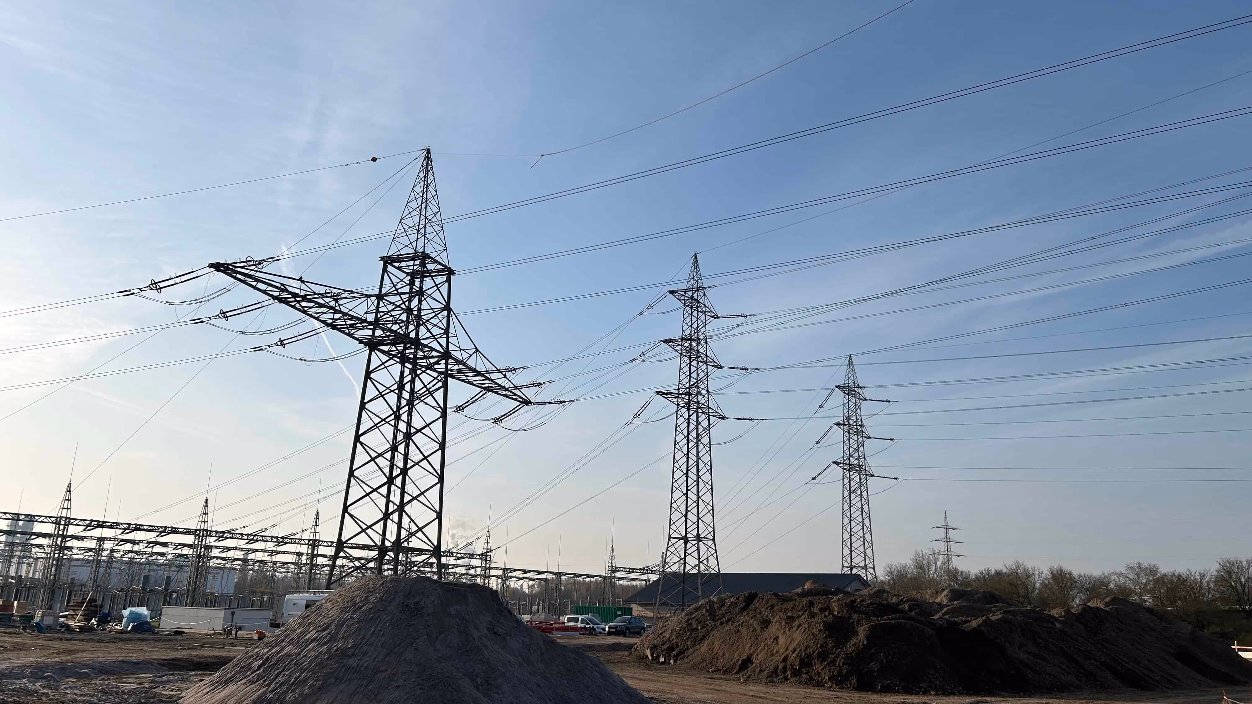 Linie wysokiego napięcia i słupy energetyczne na terenie budowy z kopcami ziemi pod niebieskim niebem.