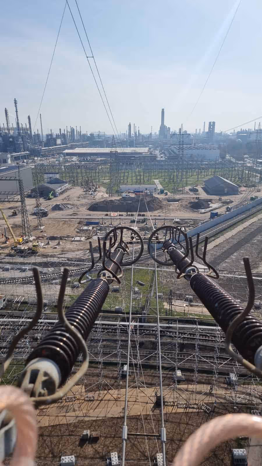 Widok na stację energetyczną z wysokiego napięcia zbliżenie na izolatory i linie przesyłowe w tle instalacje przemysłowe i plac budowy.