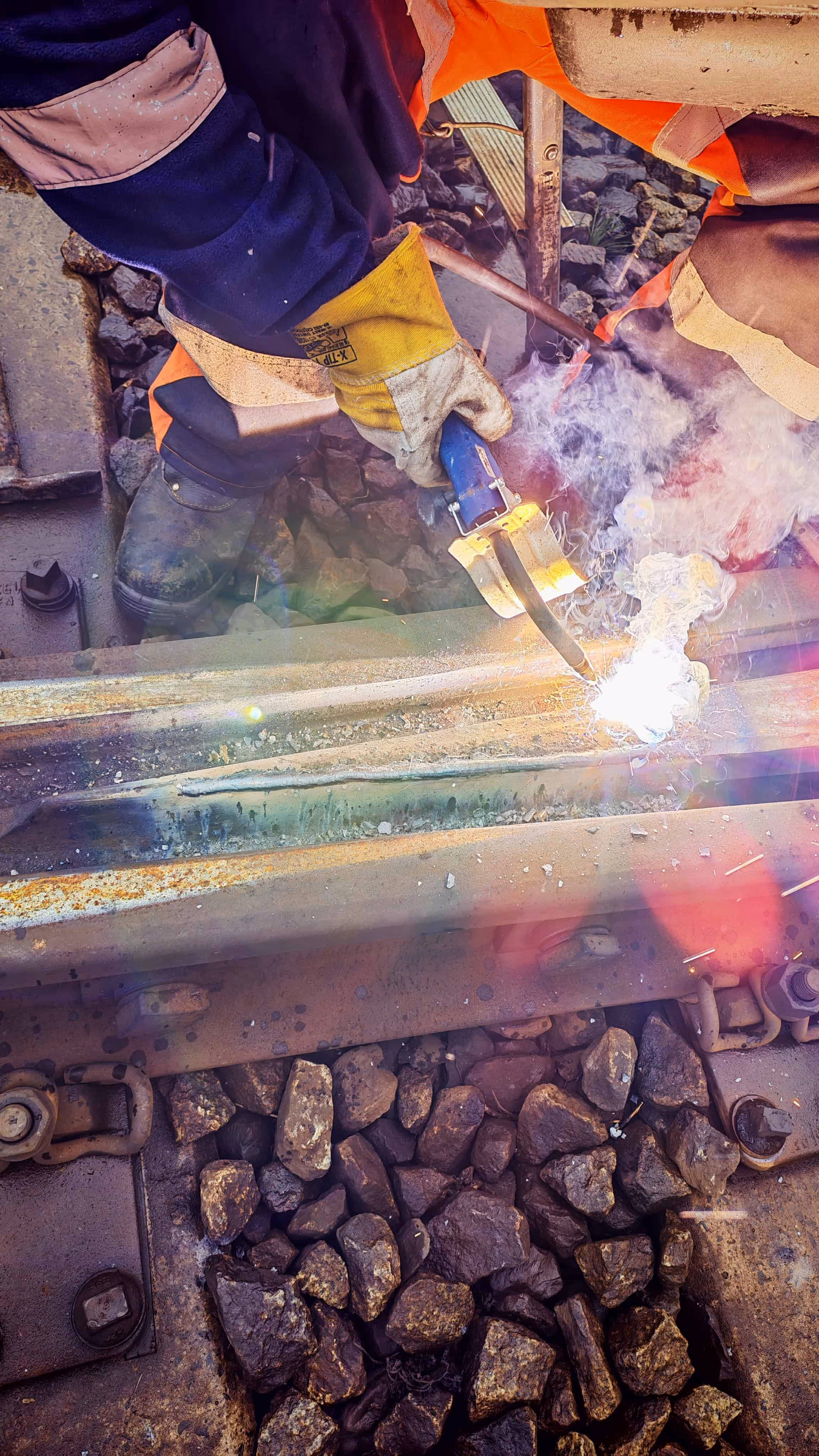 Pracownik w odzieży ochronnej spawający szynę kolejową na torach.