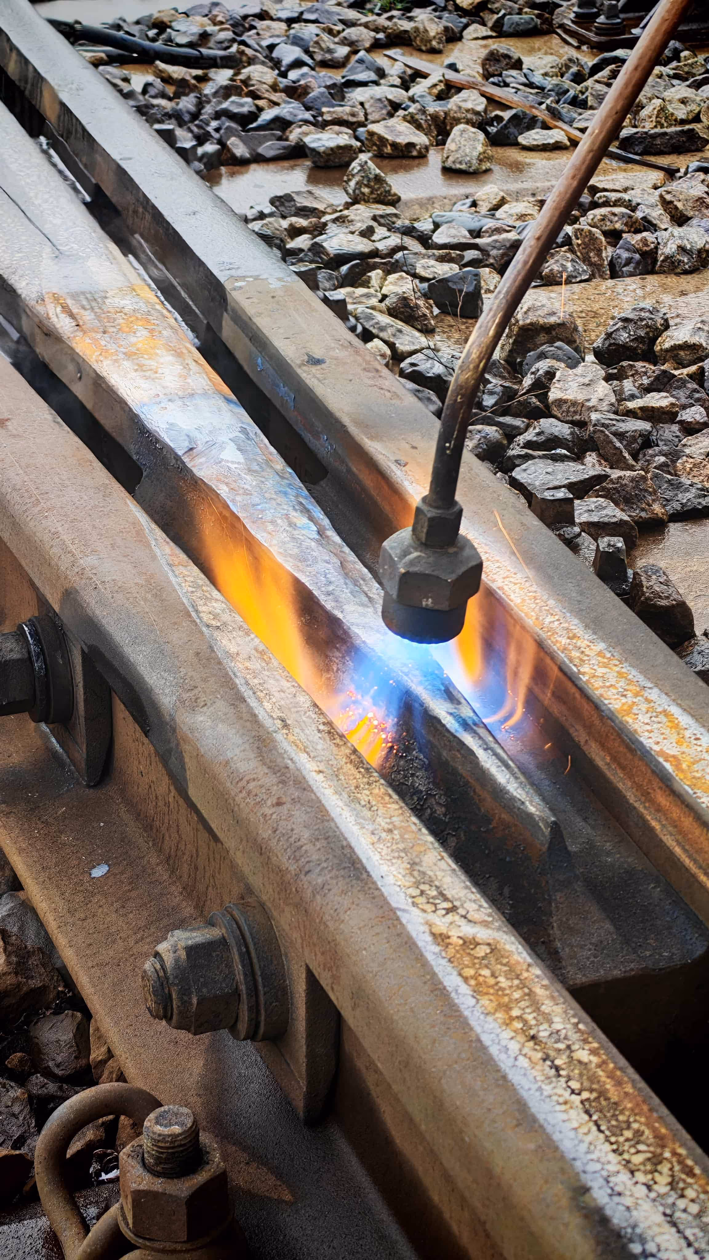 Płomień spawalniczy wygładzający metalowy szynę kolejową na podsypce z kamieni.