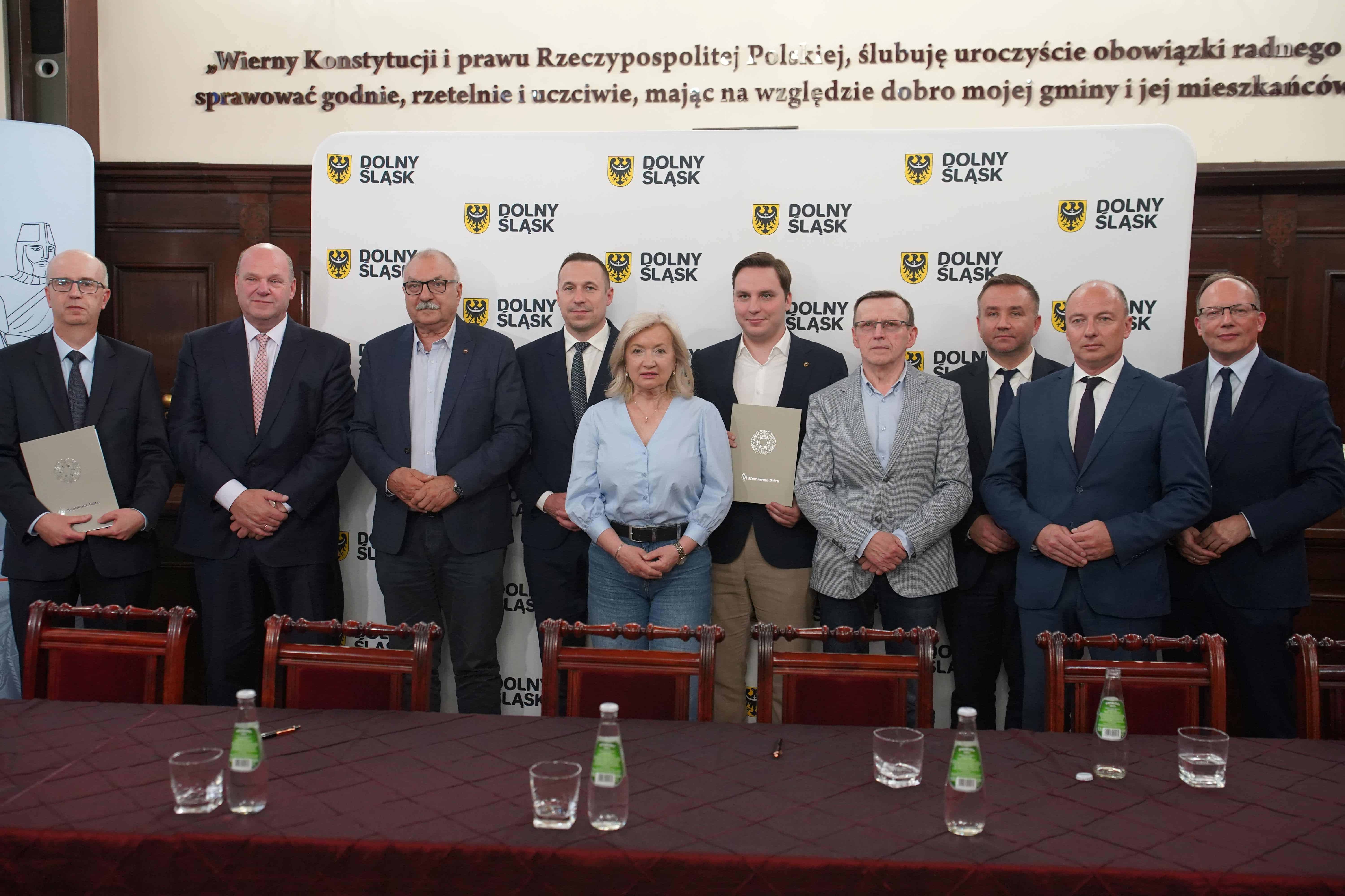 Dziesięć osób pozujących przed ścianką Dolny Śląsk za stołem z wodą i szklankami.