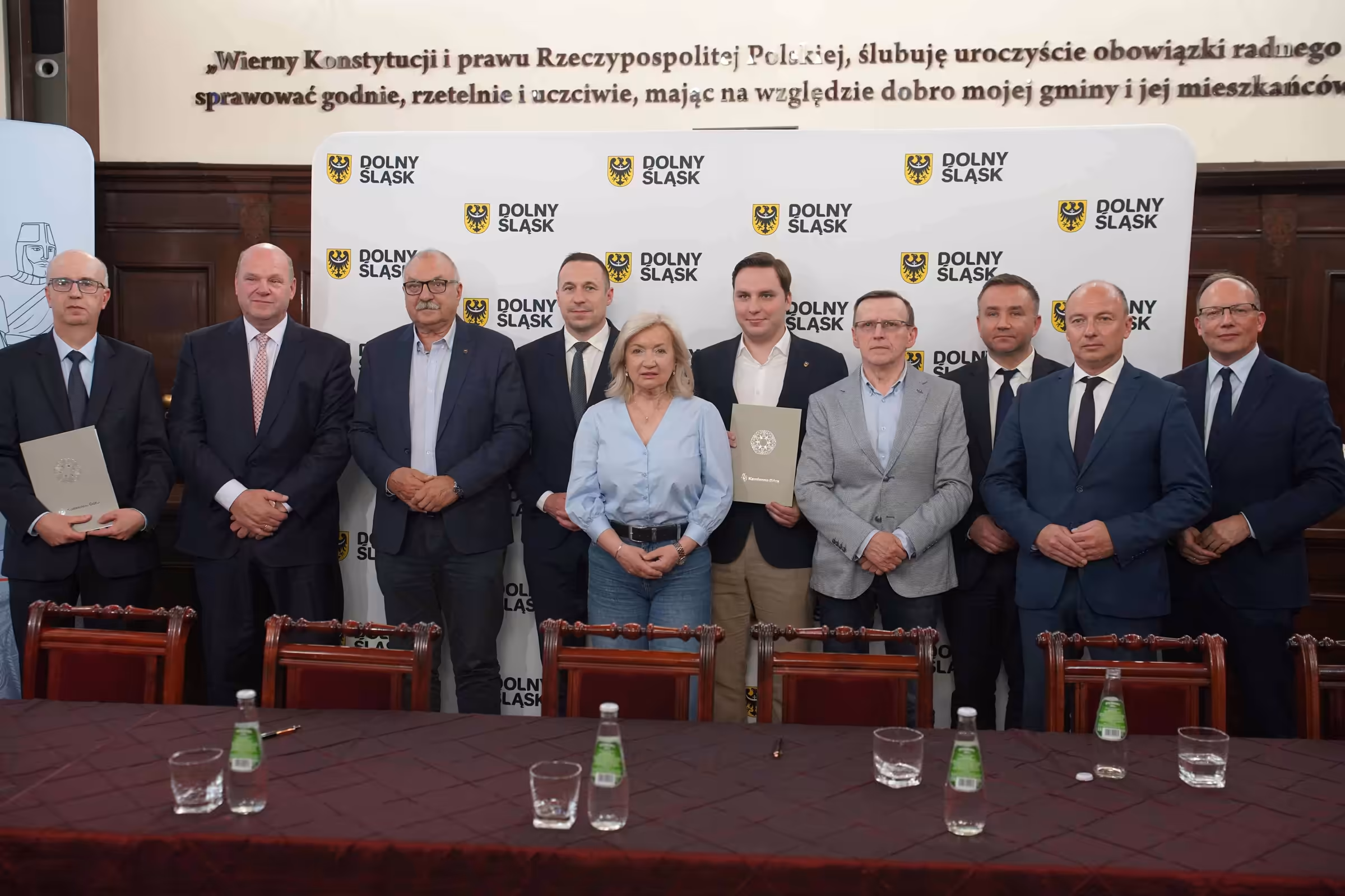 Uczestnicy podpisania umowy na rewitalizację linii Kamienna Góra–Ogorzelec pozują przed ścianką Dolnego Śląska.
