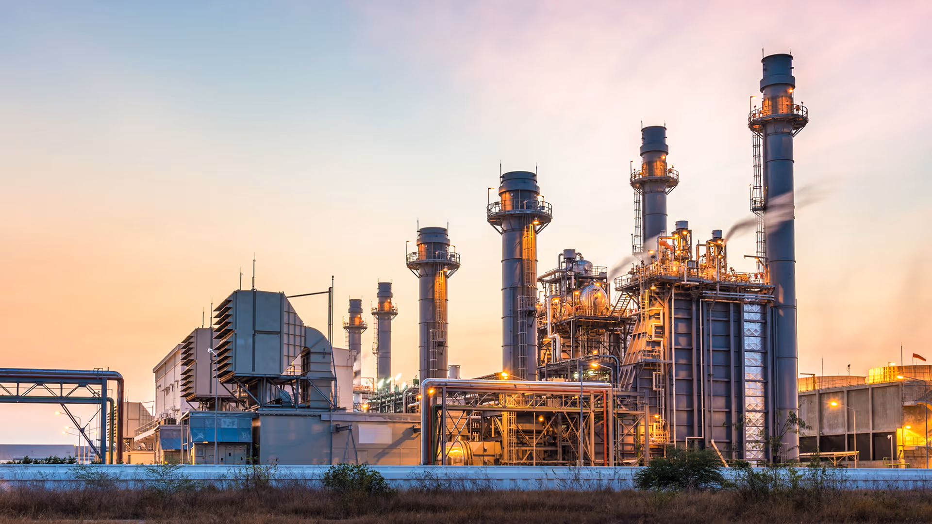 Industrial power plant with large chimneys and machinery at sunset.
