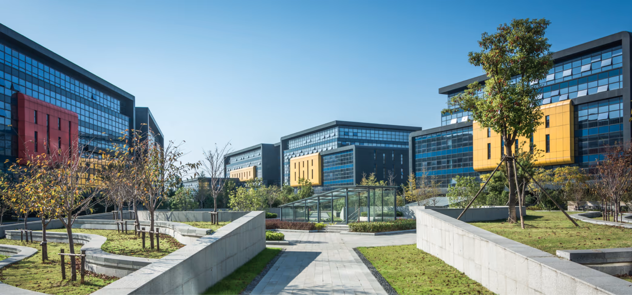 Modern corporate campus with glass office buildings, landscaped green spaces, and a clear blue sky.