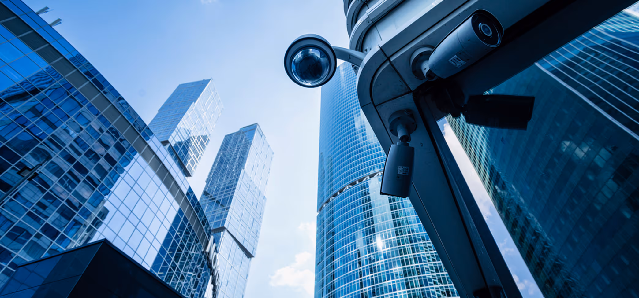 Low-angle view of modern glass skyscrapers with multiple security cameras mounted on a building corner.