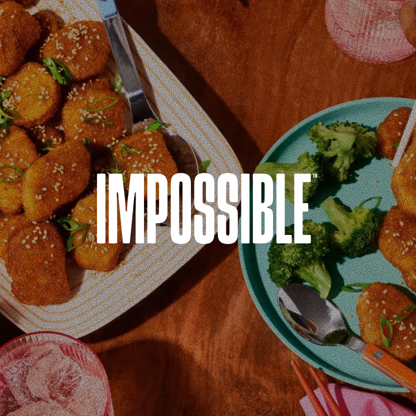Plates of sesame-coated nuggets garnished with green onions and broccoli on a wooden table with the word Impossible overlayed.