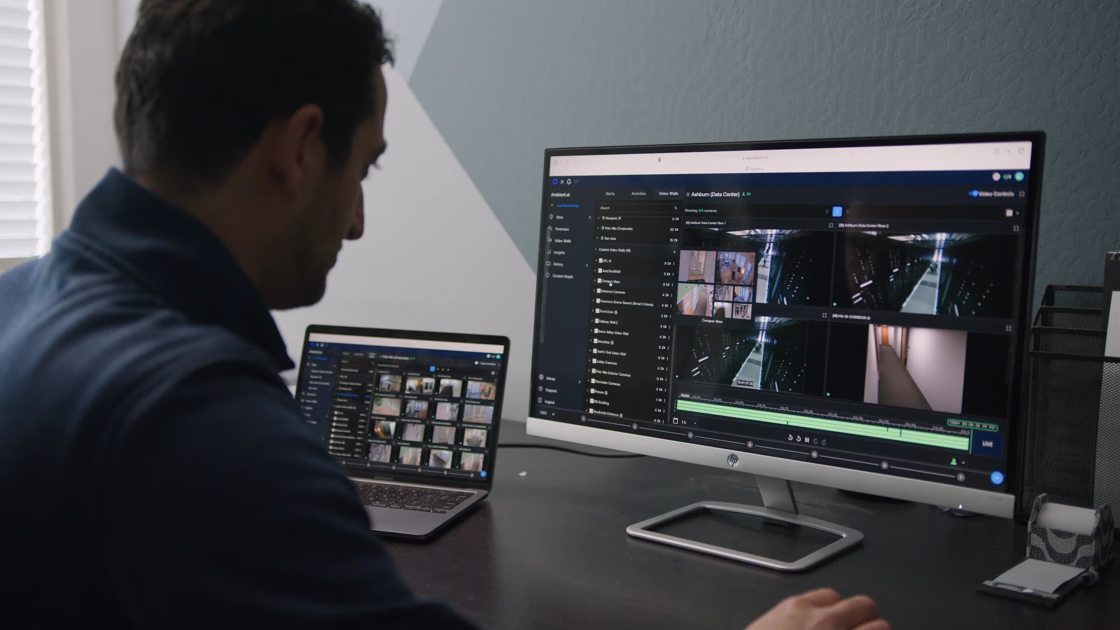 Person monitoring multiple security camera feeds on a desktop monitor and laptop screen at a desk.