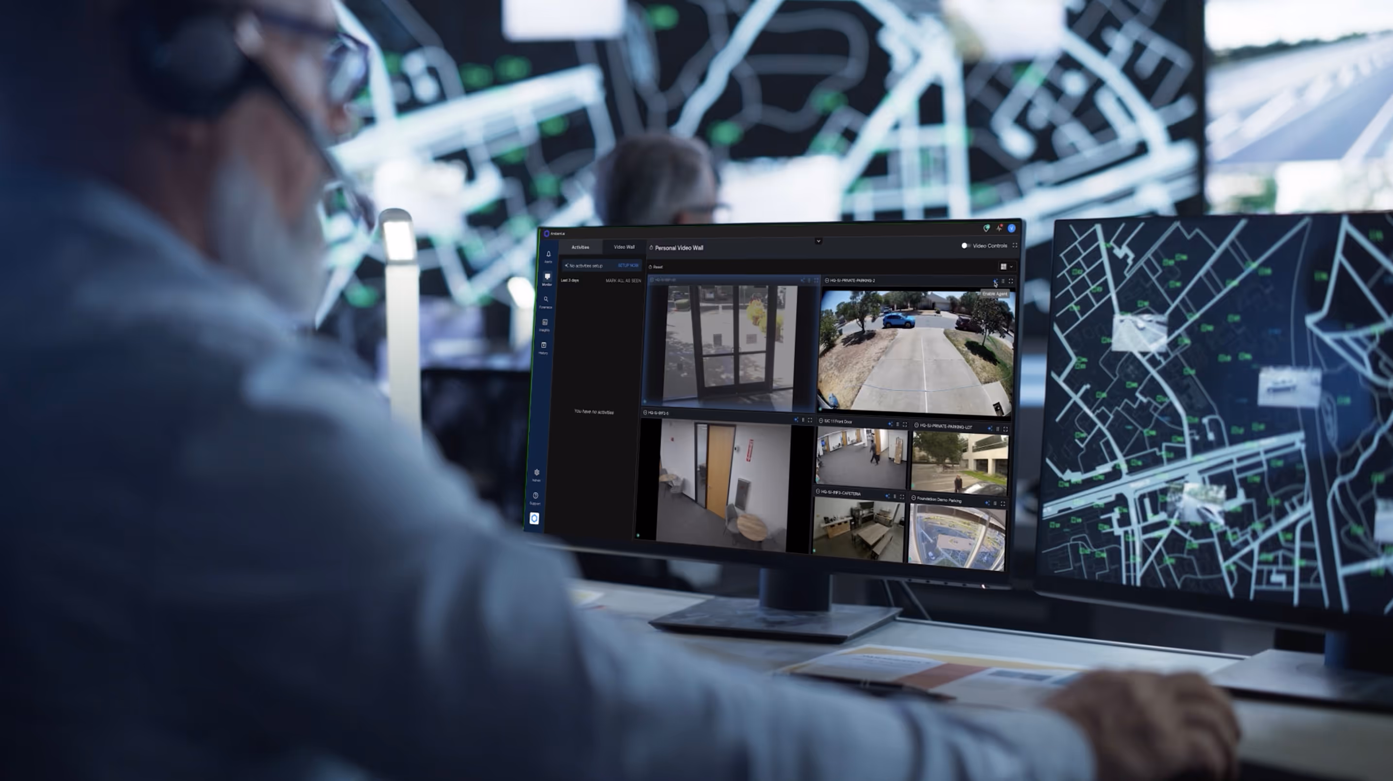 Person wearing headset monitors multiple security camera feeds and a digital map on adjacent computer screens.