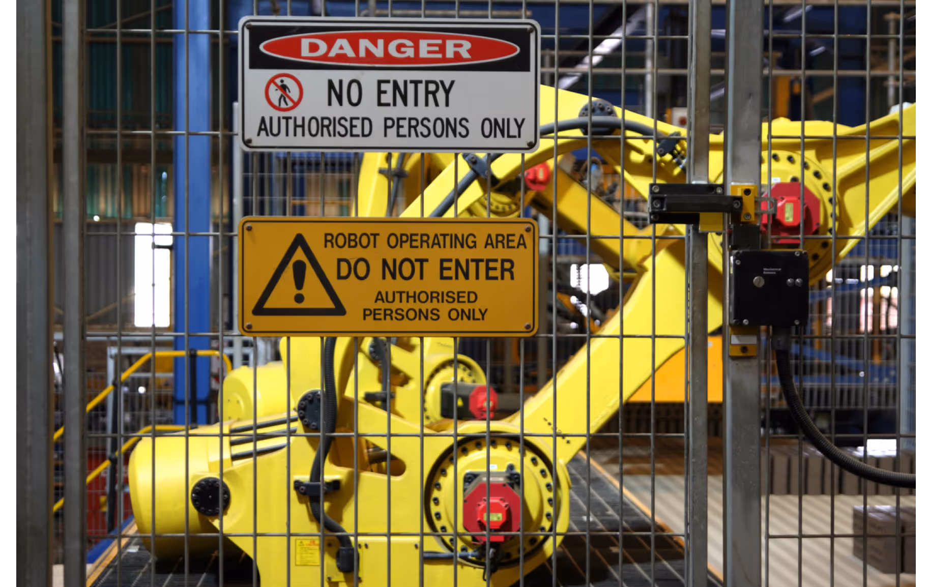Yellow industrial robot inside a fenced area with warning signs prohibiting entry to unauthorized persons.