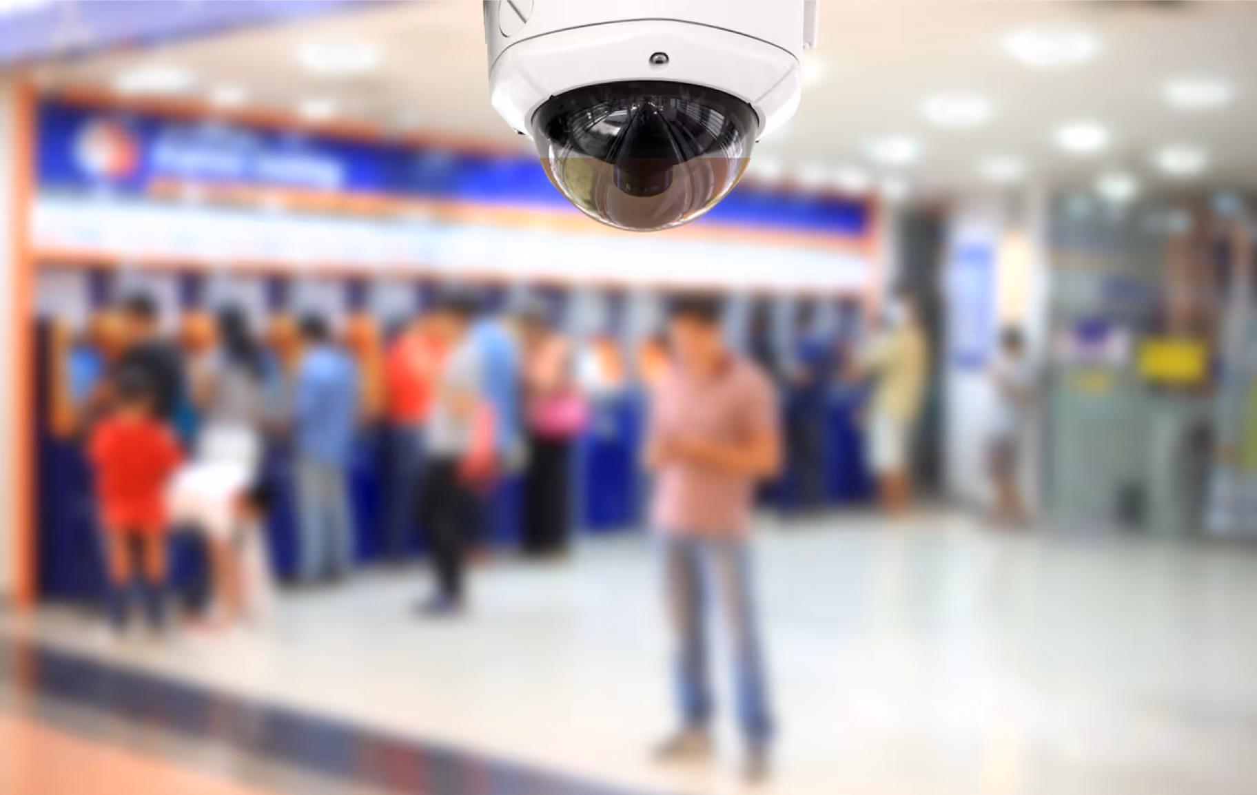 Security surveillance camera overlooking a blurred crowd of people queuing indoors.