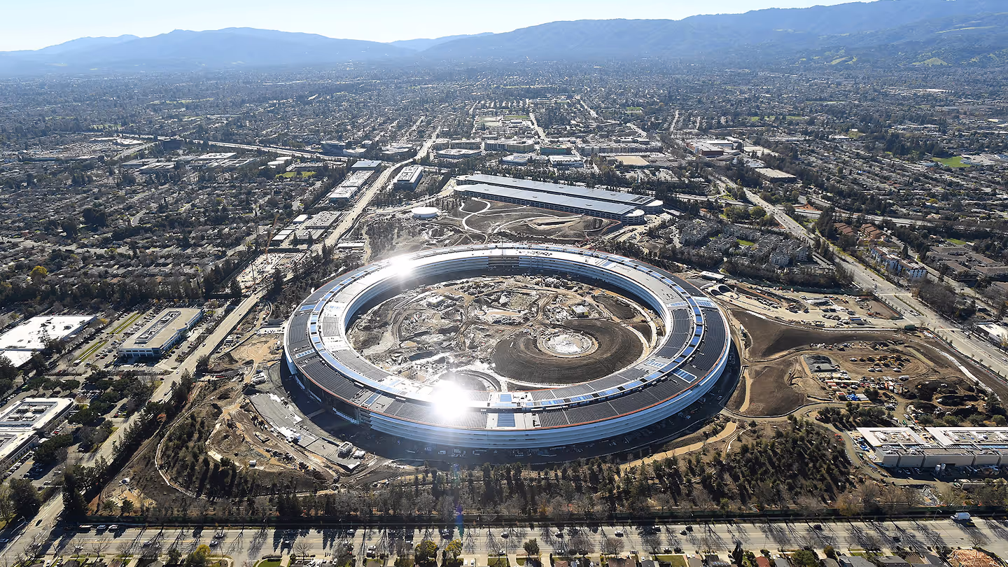 Aerial view of a large circular building under construction surrounded by roads and urban landscape.